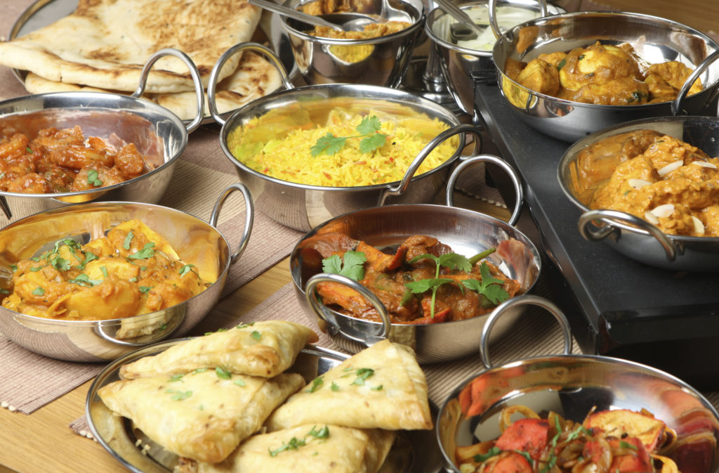 Selection of Indian food including curries, rice, samosas and naan bread.